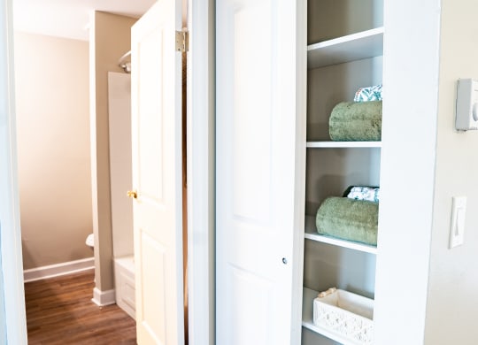 a closet with a white door and white shelves with blue and green towels