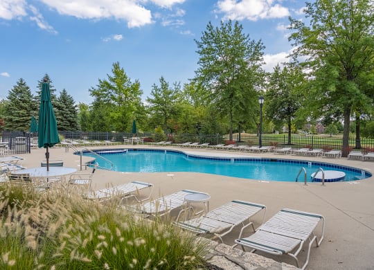 a swimming pool with chairs and umbrellas and trees at Four Bridges, Ohio