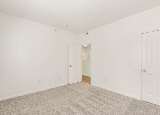 a bedroom with white walls and carpet and a door to a closet