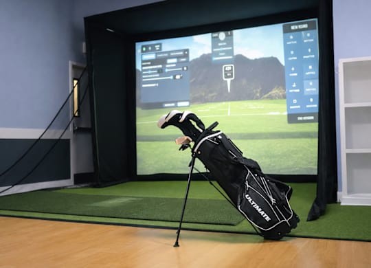 A golf bag with clubs is placed in front of a screen showing a golf game.