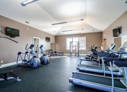 a gym with cardio machines and weights and a tv at Grove City Summit Apartments, Grove City
