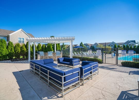 the lounge area of a pool with blue couches and a white pergola at Grove City Summit Apartments, Grove City, 43123
