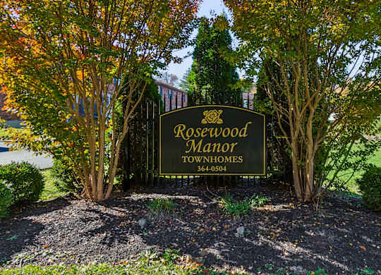 A sign for Rosewood Manor Townhomes is surrounded by trees.