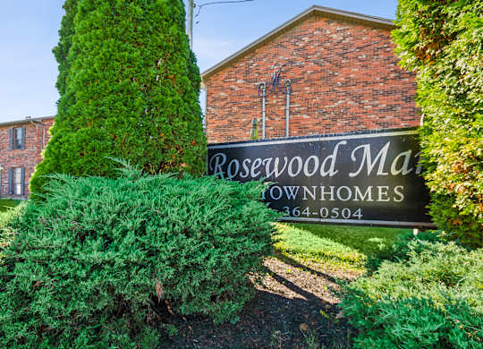 A sign for Rosewood Manor Townhomes is in front of a brick building.