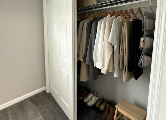 A white closet with clothes hanging and a bench underneath.
