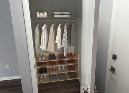 A white closet with clothes and shoes.