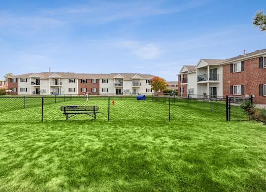 A grassy area with a bench and a fence in front of apartment buildings.
