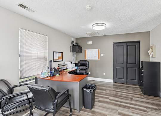 A room with a desk, chairs, and a trash can.