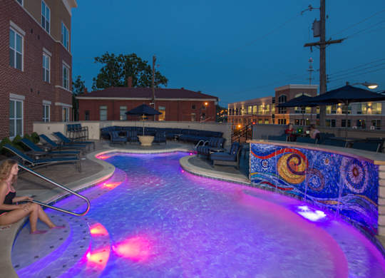 A woman sits by a lit pool at dusk.