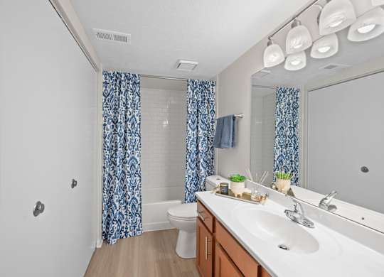 A bathroom with a white sink, a toilet, a shower curtain, and a mirror.