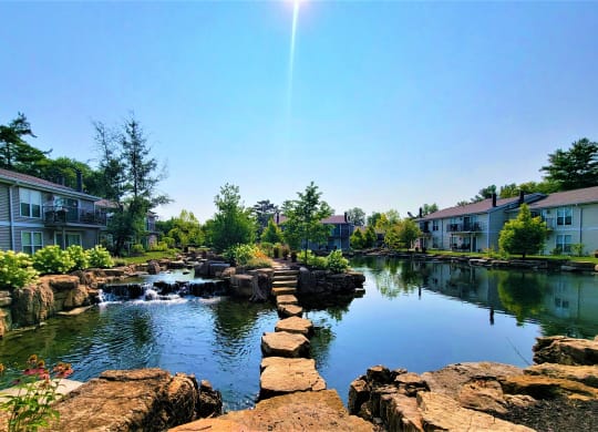 a pond with rocks and waterfall in front of an apartment complex at Harpers Point Apartments, Cincinnati, Ohio