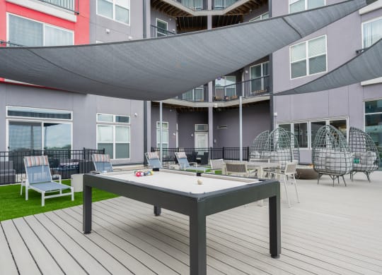 a patio with a pool table and chairs in front of a building