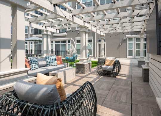 Liberty Township, OH, Apartments with In-Unit Washer and Dryer - Liberty Center - Courtyard with Pergola-Like Roofing, Cafe Lights, Couch, Stone Coffee Table, Pillars, Mounted TV, and Egg-Style Chairs.