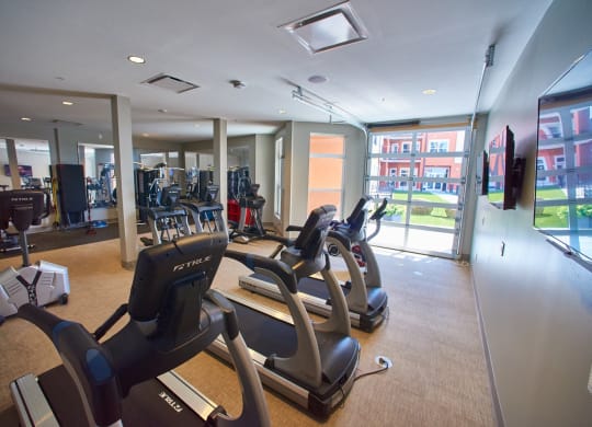 Apartments in West Chester for Rent- Liberty Center- Fitness Center with Treadmills, Floor-to-Ceiling Windows, and Mounted Televisions