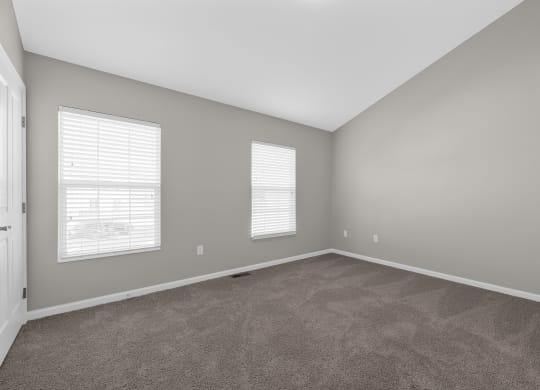 an empty living room with carpet and two windows at Traditions at Slate Ridge, Reynoldsburg, OH
