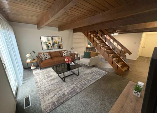 A living room with a brown couch and a wooden staircase.