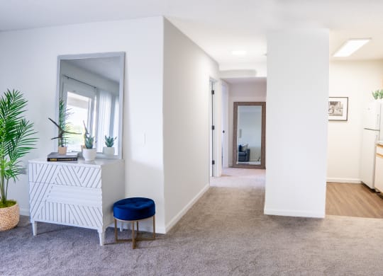 a hallway with white walls and a white dresser with a blue stool