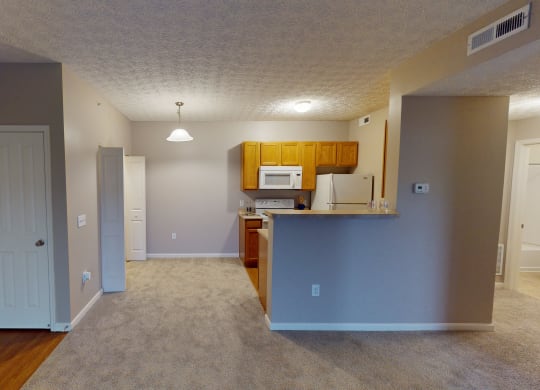 an empty living room with a kitchen and a door to a hallway