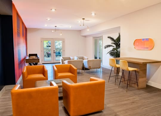 a seating area with orange chairs and a bar