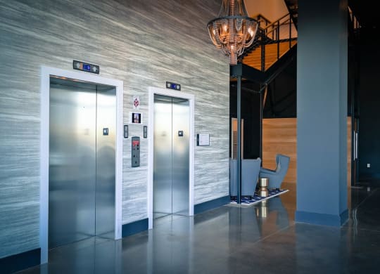 a lobby with three elevators and a chair and a chandelier