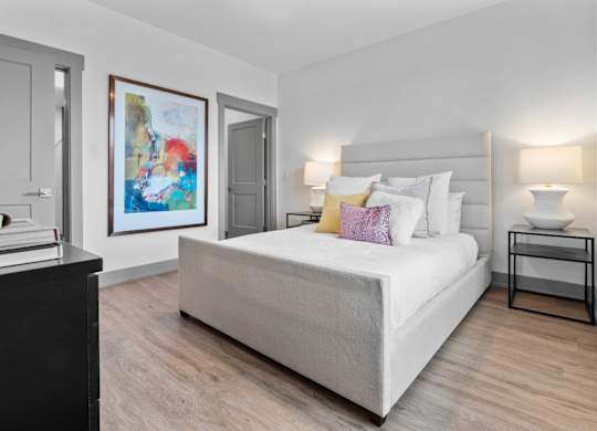 A bedroom with a large bed, a nightstand, and a painting on the wall. at The Ridge Apartments, Cincinnati, OH