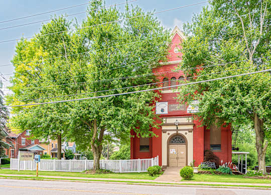 A red brick building with a white clock tower stands in front of a green tree. at The Ridge Apartments, Cincinnati