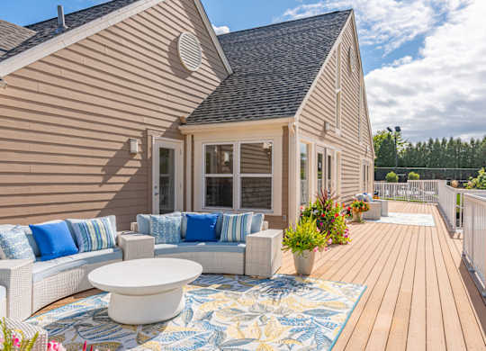 A house with a wooden deck and a white couch with blue pillows.