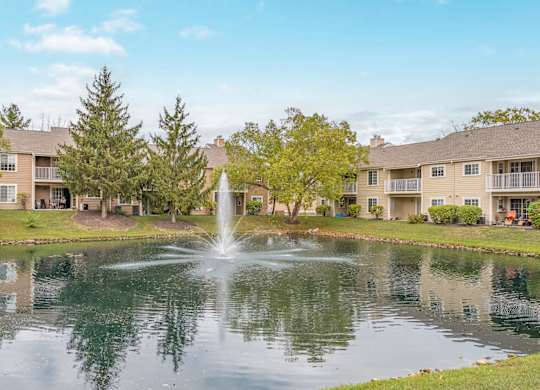 A fountain in the middle of a pond in front of apartment buildings.