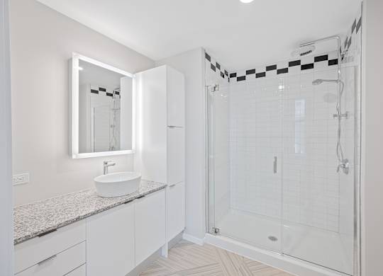 A white bathroom with a sink, mirror, and shower at Sky Central Apartments, Cincinnati, Ohio