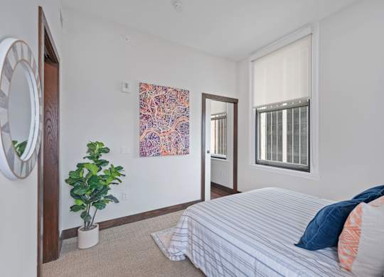 A bedroom with a bed, a plant, and a painting on the wall at Sky Central Apartments, Cincinnati, OH, 45202