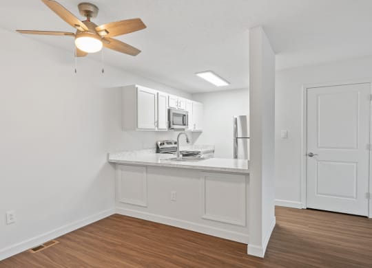an open living room with a kitchen and a ceiling fan