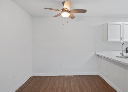 an empty living room with a ceiling fan and a kitchen