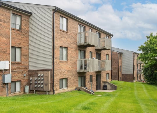 a brick apartment building with balconies and a green yard at The Woodridge Collection, Fairfield, OH 45014