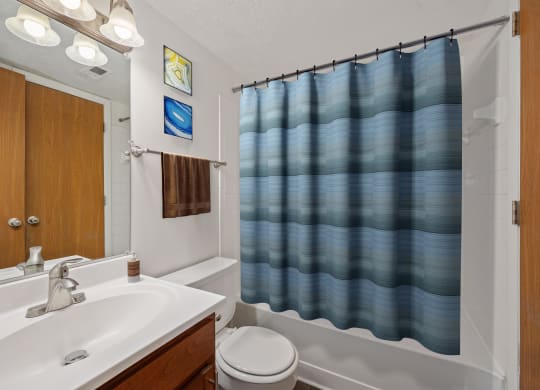 a bathroom with a white sink and a blue shower curtain at The Woodridge Collection, Fairfield, OH 45014