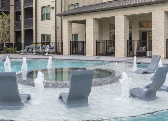 a pool with chairs and a fountain in front of a building