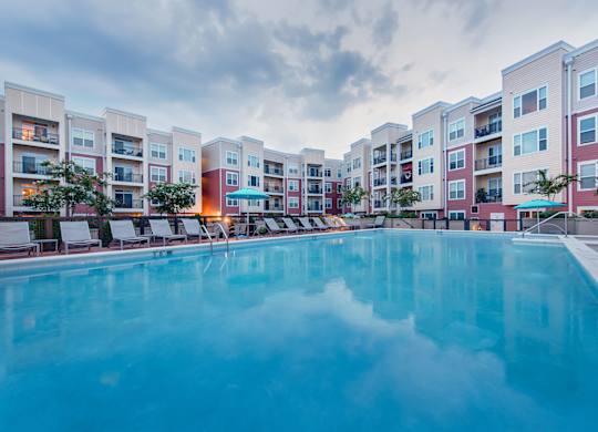 a swimming pool with lounge chairs and umbrellas in front of an apartment building