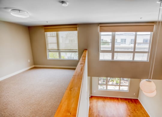 an empty living room with three large windows and a wooden railing