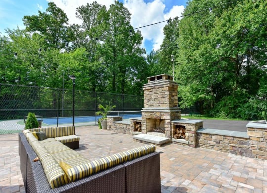 Windsor Oak Creek - Courtyard with a stone fireplace and a tennis court in the background in Fairfax VA