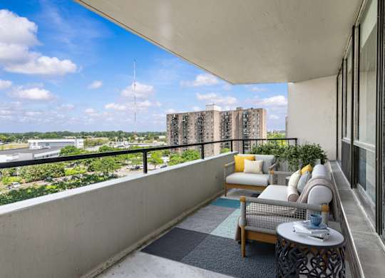 A balcony with a couch, chairs, and a table overlooking a cityscape.