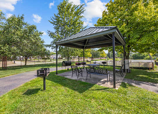 A covered picnic area with tables and chairs is surrounded by trees.