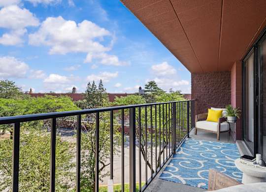 A balcony with a blue patterned carpet and a white pillow.