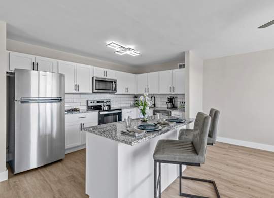 A modern kitchen with a stainless steel refrigerator and a marble island.