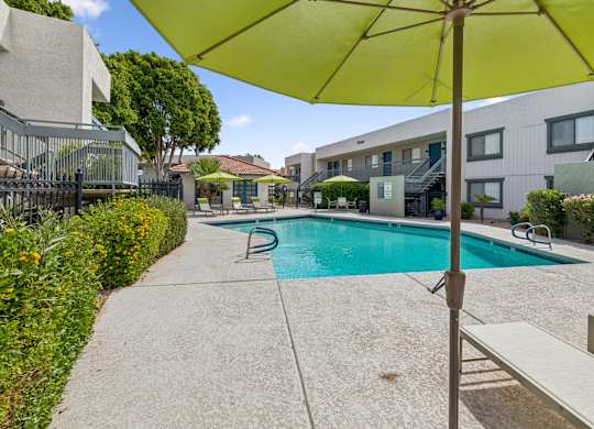 A pool surrounded by a concrete patio and a yellow umbrella.