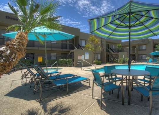 A poolside area with a table, chairs, and umbrellas.