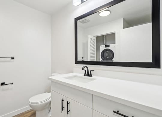 A bathroom with a white countertop and a mirror reflecting a fan.