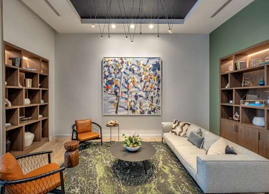 A living room with a large abstract painting on the wall, a grey sofa, a coffee table, and two chairs.