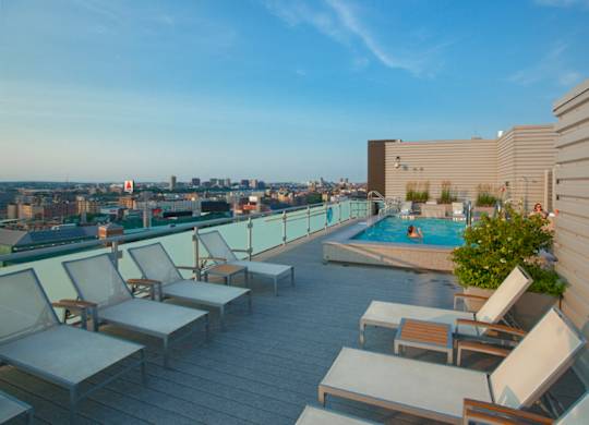 A rooftop patio with chairs and a pool overlooking a city skyline.