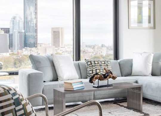 A living room with a grey couch and a city view through the window.