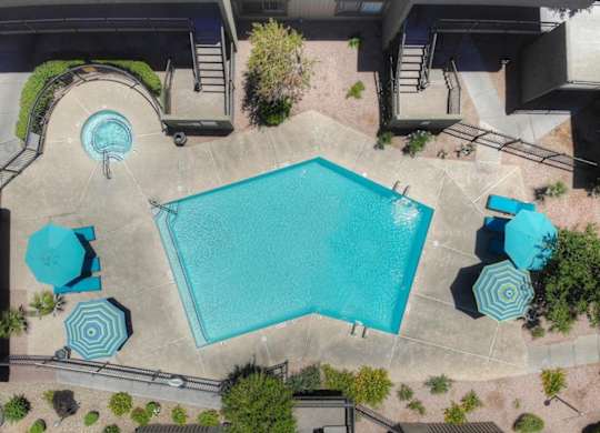 An aerial view of a swimming pool surrounded by a concrete patio and a brick wall.