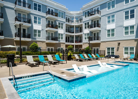 a swimming pool with lounge chairs in front of an apartment building